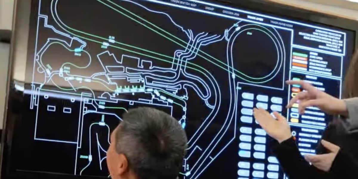 People are discussing in front of a large screen displaying a diagram of Radiator Springs Racers. 