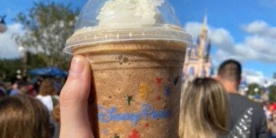 Someone holding a Starbucks drink in front of Cinderella Castle at Walt Disney World Resort.