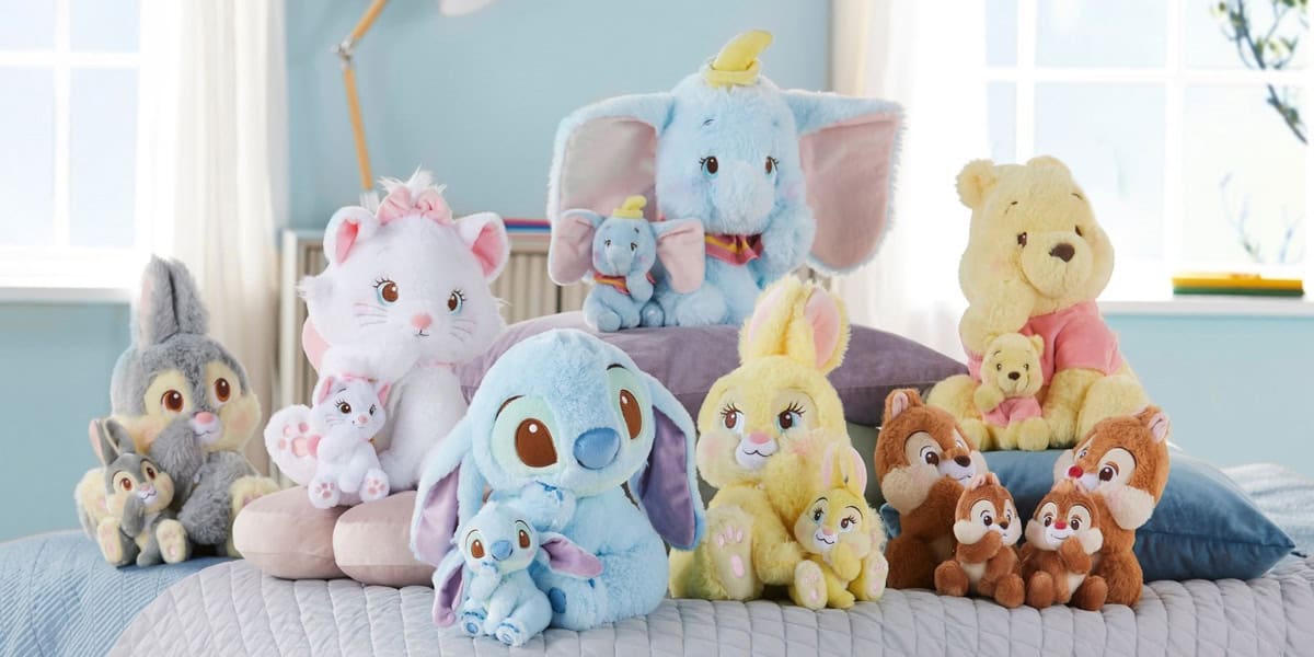 A collection of cute plush toys and key chains from Japan are nestled on a bed. These delightful Disney Store offerings showcase fluffy creatures in pastel hues like blue, yellow, and cream, with some charmingly holding smaller plush versions of themselves.