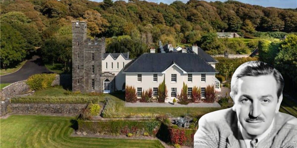 A large, elegant house with a blend of traditional and modern architecture reminiscent of a Disney Castle is surrounded by lush greenery and trees. Listed for sale for the first time in 35 years, its charm is accentuated by a black-and-white cutout of a man with a mustache in the foreground.