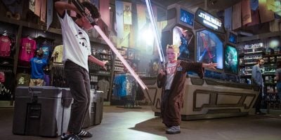 Two children playfully engage in a lightsaber duel in a Star Wars-themed store.