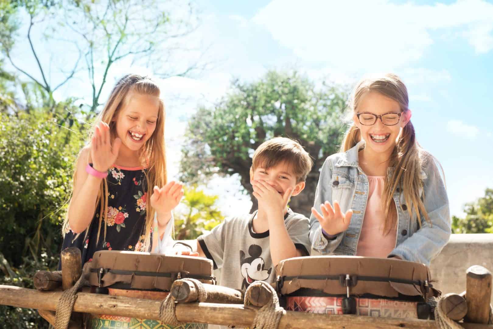 Two young girls and a young boy smile as they play drums at Disney's Animal Kingdom