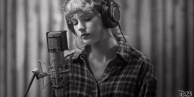 A person wearing headphones sings or records into a microphone in a studio, evoking the vibe of Taylor Swift masters sessions. They have wavy hair, wear a plaid shirt, and stand against a softly blurred black and white background.