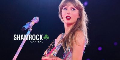 A woman with long blonde hair, resembling Taylor Swift, performs on stage with a guitar and sparkly dress. A microphone stands before her, while the text "SHAMROCK CAPITAL" and a green clover logo appear on the left side.