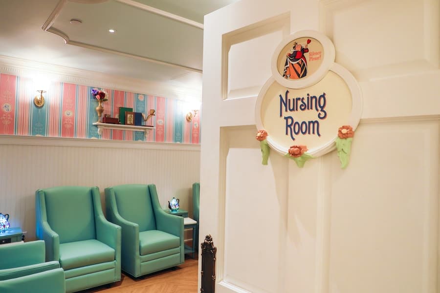 A cozy Disney Baby Care Center nursing room with several teal armchairs, soft lighting, pastel wallpaper, and a sign on the door reading "Nursing Room" with floral decorations ensures a welcoming guest experience for families.
