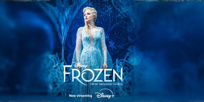 A woman dressed as Elsa in a sparkling blue gown stands confidently on a stage surrounded by icy, blue scenery. The text reads: "Frozen The Broadway Musical – the hit Broadway show now streaming on Disney+.