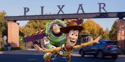 Woody and Buzz Lightyear, animated characters from Toy Story, appear in front of the Pixar Animation Studios entrance, featuring large letters spelling "PIXAR" on a metal arch above the gates, where Pixar offers guided studio tours.