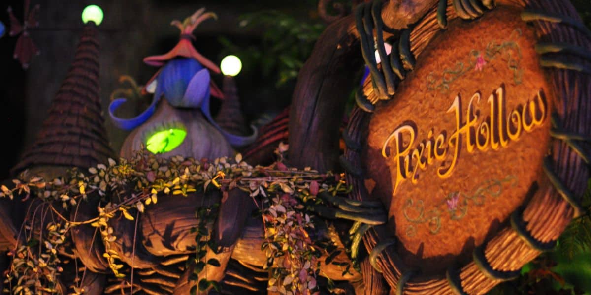 A whimsical wooden sign reading "Pixie Hollow" sits among leafy branches, while a fairy-tale house with pointed rooftops and a glowing green window hints at a magical Disneyland Meet and Greet returning soon.