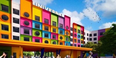 A colorful Universal building in Texas features vibrant square and circular windows, a yellow canopy, and people gathered outside; trees and birds fill the bright theme park sky.