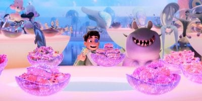 A boy and a smiling creature sit behind glowing bowls of colorful, sparkly treats in a whimsical, brightly lit setting reminiscent of Disney Parks, with fantasy characters and floating objects in the background.