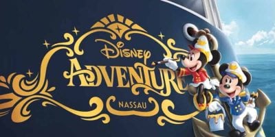 Disney Adventure Nassau logo in gold lettering on a ship's dark blue hull, with Minnie and Mickey Mouse dressed in sailor uniforms, smiling, and waving near the ocean on a sunny day.
