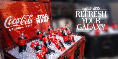 A red chest filled with ice and Coca-Cola bottles featuring Star Wars branding celebrates the Refresh Your Galaxy campaign. The background displays "Coca-Cola Star Wars Refresh Your Galaxy" in bold white letters, uniting Coca-Cola and Disney magic.