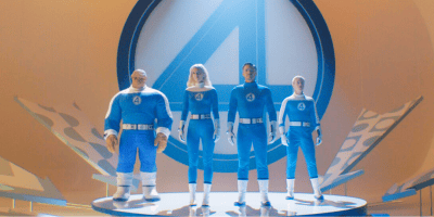 Four people in blue superhero suits with white gloves and boots stand on a platform before a large number 4 symbol—the iconic Fantastic Four, now set to join the MCU under Disney’s banner. Three are human, one is a large, rocky humanoid.