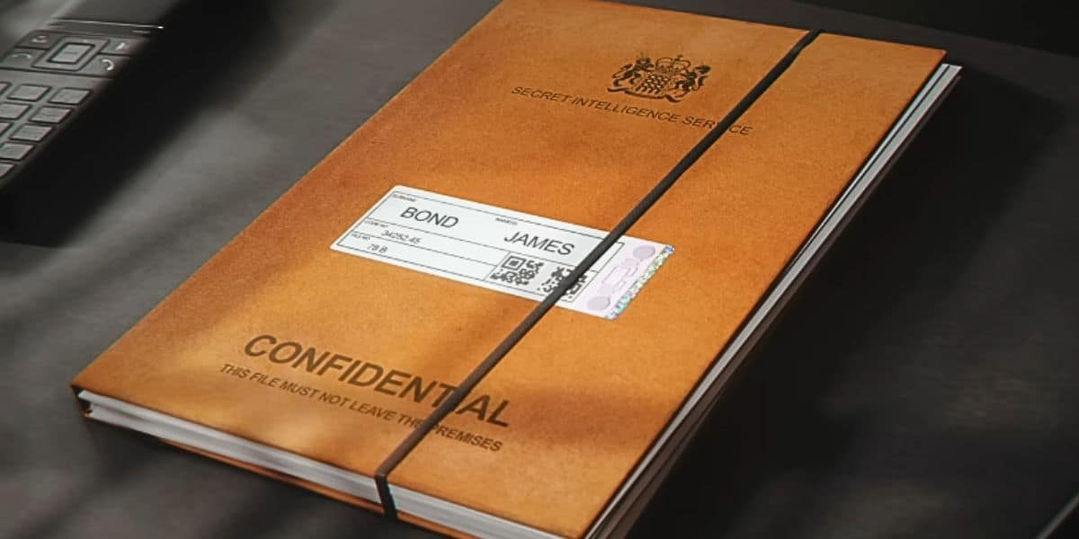 A brown folder labeled "CONFIDENTIAL" and "SECRET INTELLIGENCE SERVICE" lies on a desk, secured with a black elastic band; a label reads "Bond, James Bond. Taken from the "007 First Light" trailer