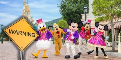 Disney characters in colorful costumes pose on a park street, while a large yellow "WARNING" sign hints at an emerging disturbance, possibly linked to a Disney Resort shutdown or vacations on hold, partially blocking the view at this Disney Resort.