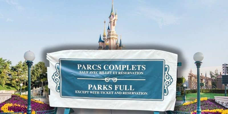 A sign in front of a castle reads "Parks Full Except With Ticket and Reservation" in English and French. The background shows a bright, sunny day at a theme park with clear skies and greenery at this Disney Resort.