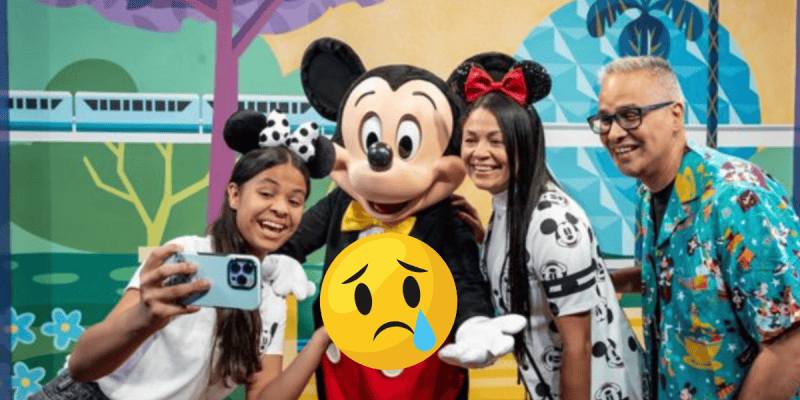 A family poses for a selfie with a person in a Mickey Mouse costume at Disney World. A large, sad-faced emoji with a tear covers the center, hinting at problems or external factors affecting their visit.