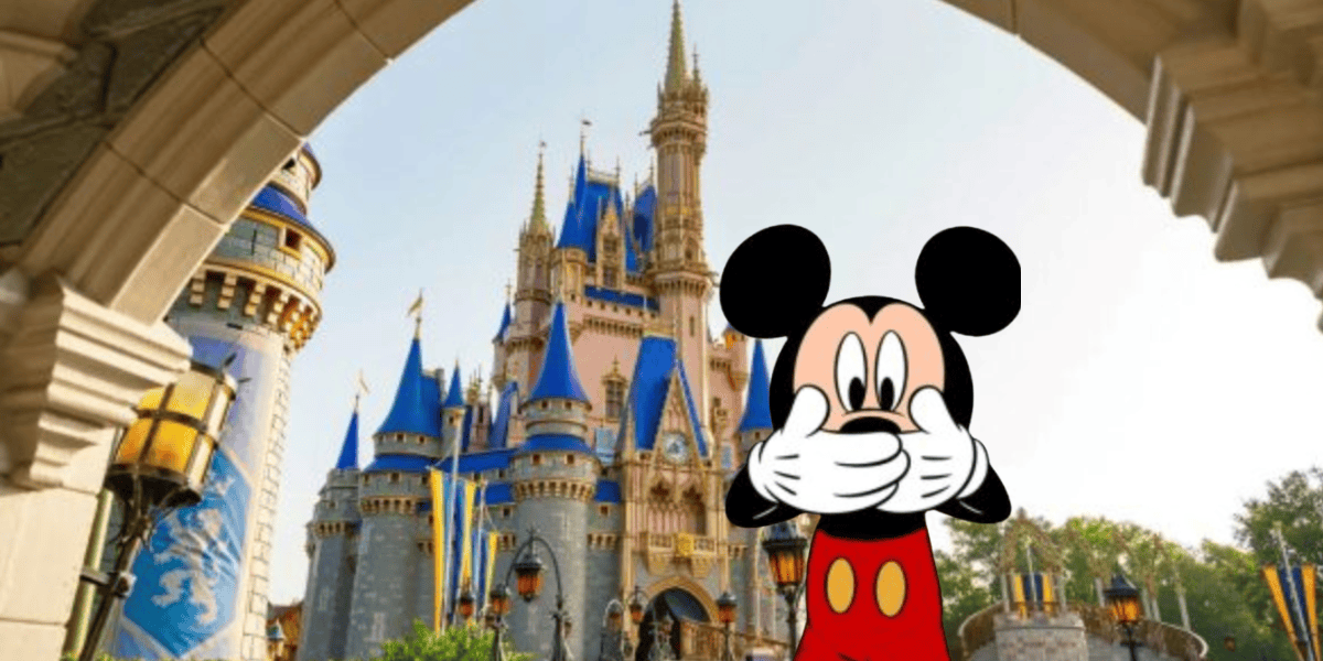 Mickey Mouse stands in front of Cinderella’s Castle at a Disney World Hotel, covering his mouth with both hands, framed by a stone archway with lanterns.