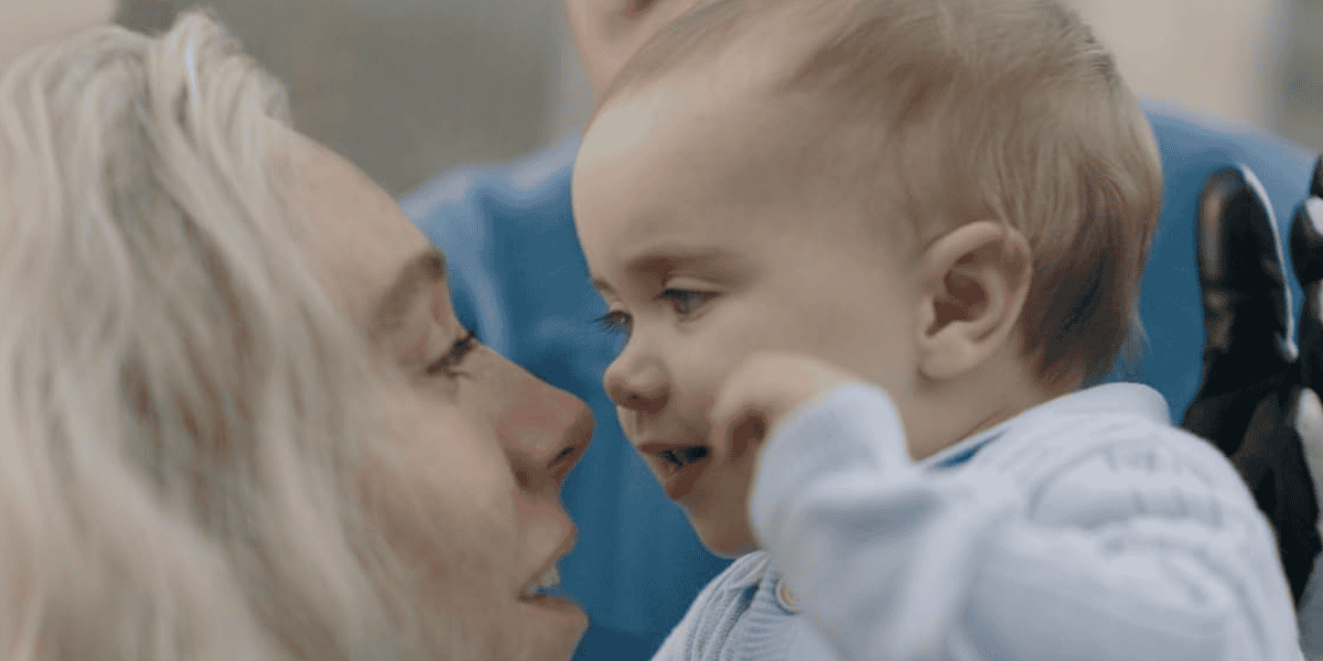 A close-up of an adult with light hair smiling and touching noses with a baby in a light blue outfit, reminiscent of the warmth seen in MCU moments. The baby looks happy and reaches toward the adult's face.