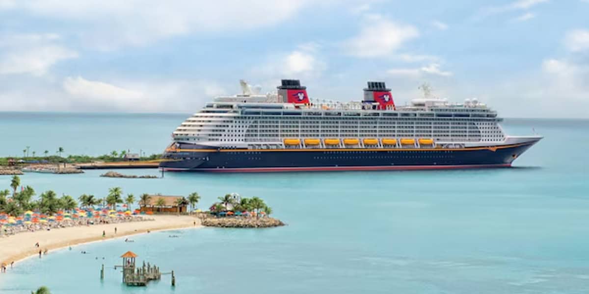 The Disney Fantasy makes its historic debut, sailing near a tropical island with palm trees, sandy beaches, and colorful umbrellas under a partly cloudy sky near Palma de Mallorca.