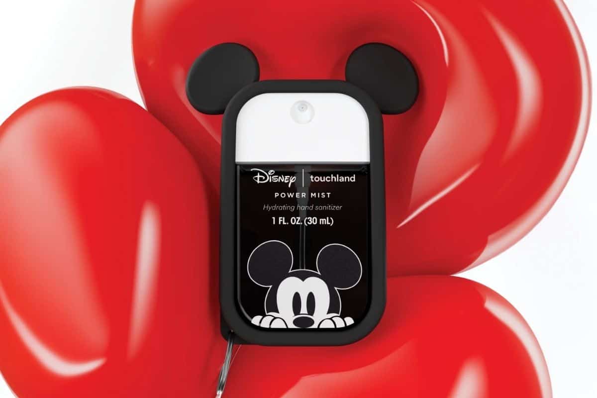 A Disney Touchland Power Mist hand sanitizer with Mickey Mouse design is placed in front of shiny red balloon shapes.