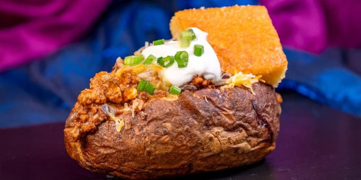 Celebrate with a Disneyland 70th Anniversary baked potato topped with chili, shredded cheese, sour cream, and green onions, paired with a square of cornbread—one of the limited-time treats from Disneyland food celebrations!.