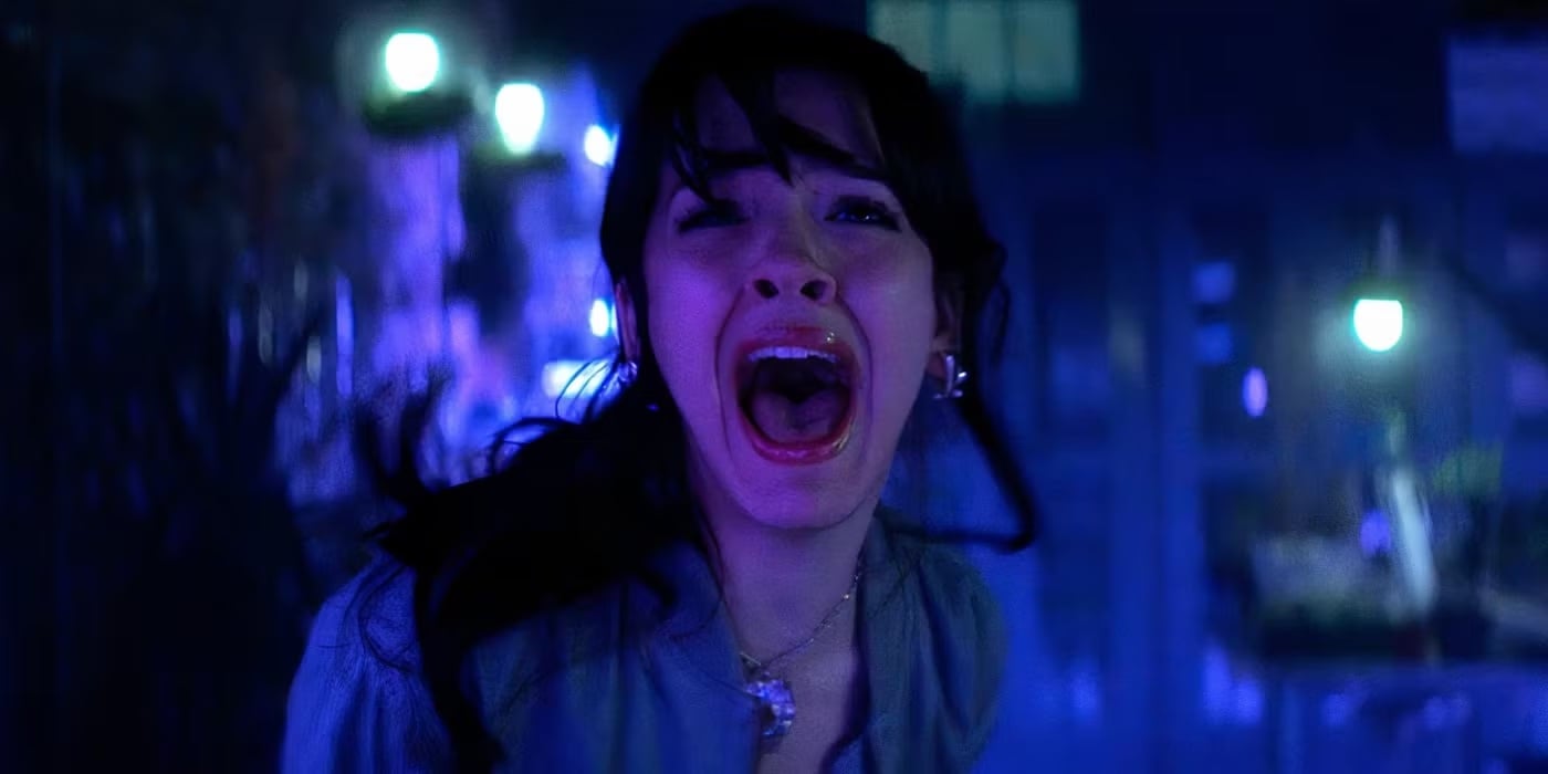 A woman with dark hair screams in terror at night, illuminated by blue and purple lighting, reminiscent of a dramatic scene from a canceled Disney+ series, with blurred lights and an urban background behind her.