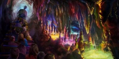 A group of people on a mine train ride through a colorful, glowing cave filled with vibrant stalactites, stalagmites, and pools reflecting various bright colors.