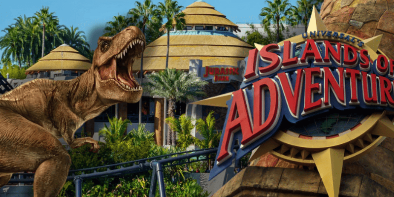 A large T. rex roars near the Jurassic Park area at Universal’s Islands of Adventure, with lush palm trees, round buildings, and the park’s red and yellow sign in the foreground at Islands of Adventure at Universal.