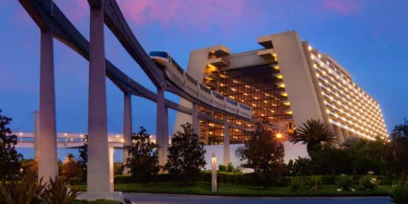 A monorail glides through a modern, A-frame resort hotel at dusk, surrounded by trees and greenery, set against a vibrant purple and blue sky.