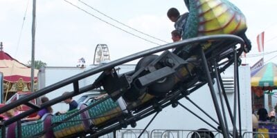Children ride a small dragon-themed roller coaster at a fair, similar to the one involved in a recent accident.