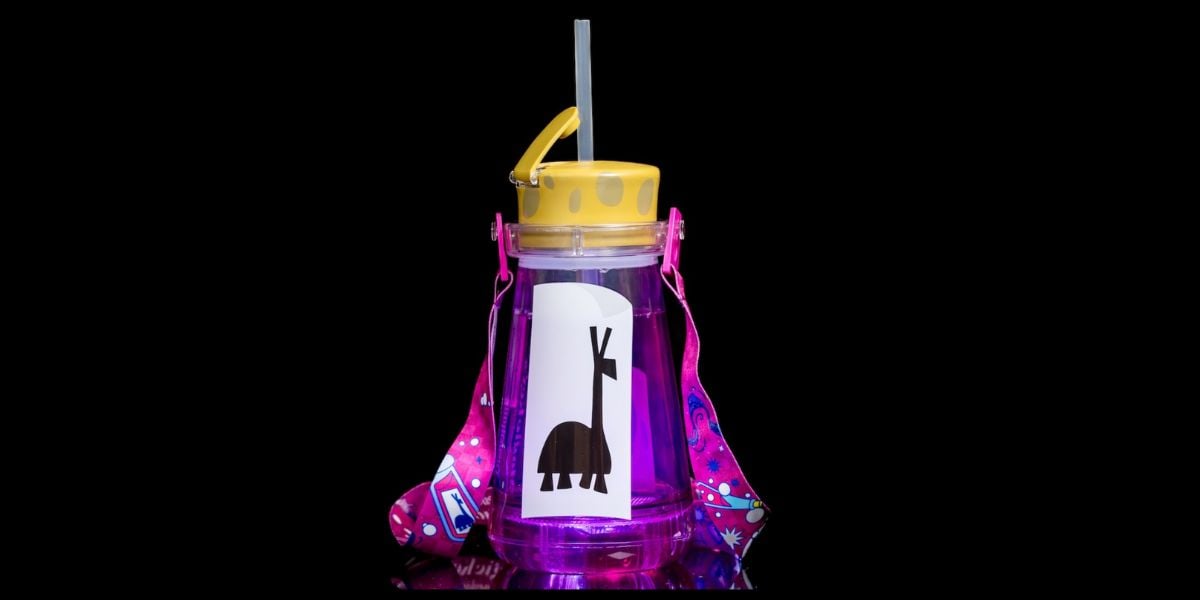 A purple sipper water bottle with a yellow lid, straw, and colorful pink strap. The bottle features a sticker of a stylized animal figure with antlers on the front, set against a solid black background.