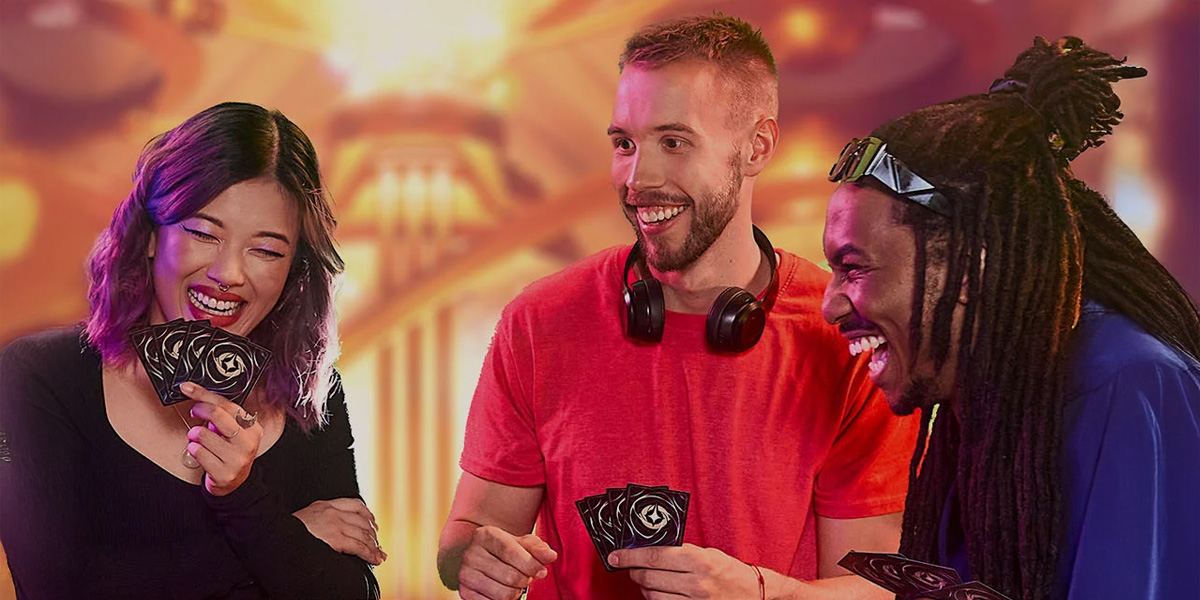 Three people are laughing and holding playing cards while gathered around a table, enjoying a game of Lorcana together. The background is warmly lit with glowing, abstract lights, celebrating the Second Anniversary with new expansions.