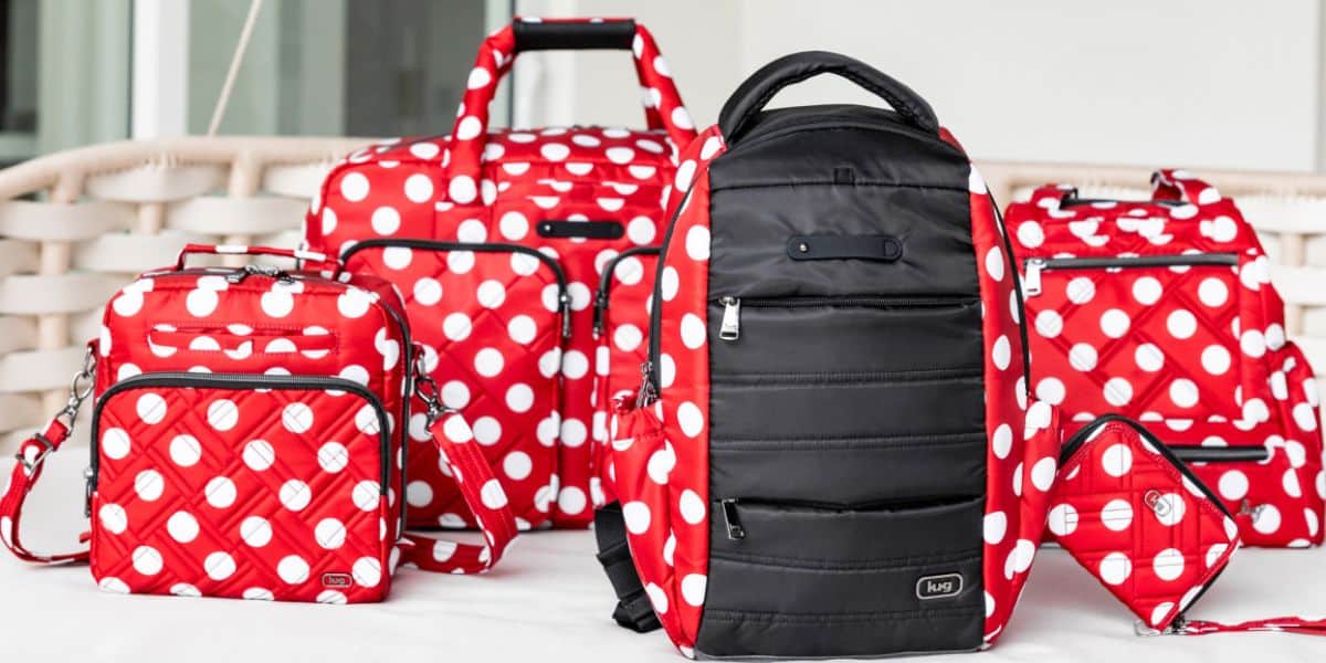 Five travel bags in red with large white polka dots and black accents are arranged together on a white surface—perfect for exclusive finds at Destination D23 2025. One bag is mostly black with red polka dot sides.