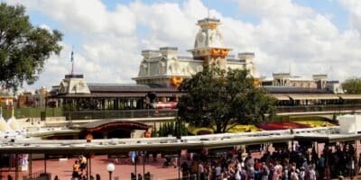 Crowds gather at the entrance of Disney’s Magic Kingdom, with the Main Street Train Station decorated for fall and Halloween.