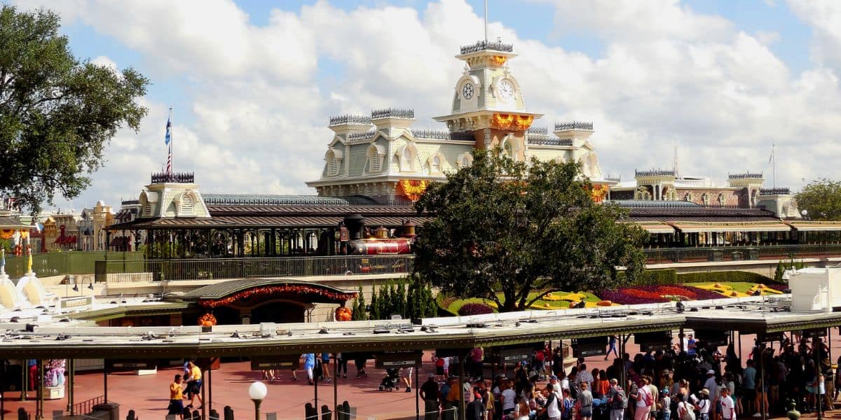 Crowds gather at the entrance of Disney’s Magic Kingdom, with the Main Street Train Station decorated for fall and Halloween.