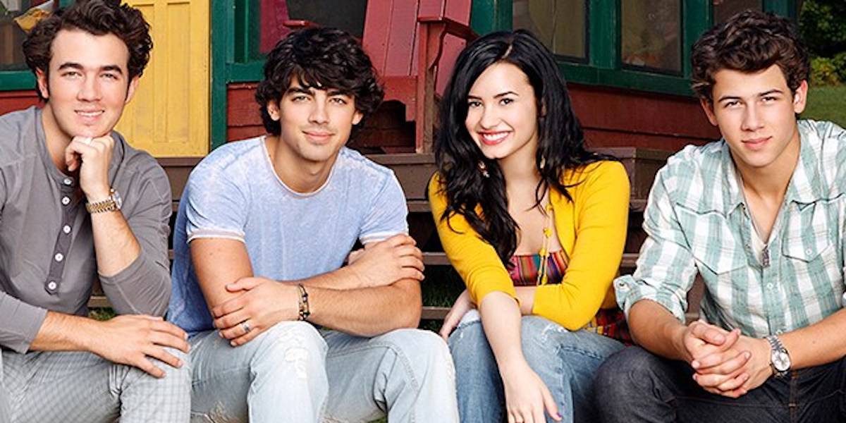 Four young people sit close together on outdoor steps, smiling at the camera. With the warmth of friends at a Spicy Wing Show, the group—three men and one woman in a yellow cardigan—appears relaxed and friendly.