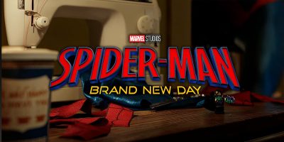A sewing machine on a wooden table with Spider-Man’s suit pieces, a coffee cup, and sewing tools. The "Marvel Studios Spider-Man: Brand New Day" logo is overlaid in the center for a first look at Tom Holland’s new Spider-Man costume.