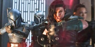 Three armored warriors, including a woman aiming a blaster, charge forward inside a futuristic corridor aglow with vertical lights. Two wear helmets—one reminiscent of the Mandalorian & Grogu era—while the woman’s face is visible, intense and determined.