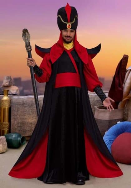 A person dressed as Jafar in a black and red sorcerer costume with a tall headpiece and staff stands outdoors at sunset, surrounded by cushions, vases, and stone decor—witchful thinking brought to life among the best Disney costumes.