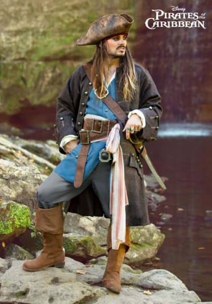 A person dressed as Captain Jack Sparrow, complete with a tricorn hat, long coat, and boots, stands on rocks by water. The "Pirates of the Caribbean" logo appears in the top right corner.