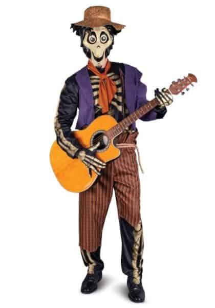 A person in a Hector skeleton costume, with a straw hat, red scarf, purple jacket, and striped pants, is holding an acoustic guitar and standing against a white background.