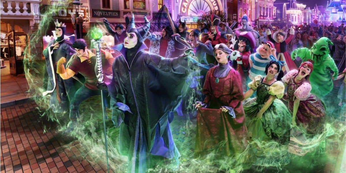 A group of notorious Disney villains, including Maleficent, Ursula, the Evil Queen, and others, gather dramatically on a glowing, enchanted street in a nighttime theme park setting with green magic swirling around them.
