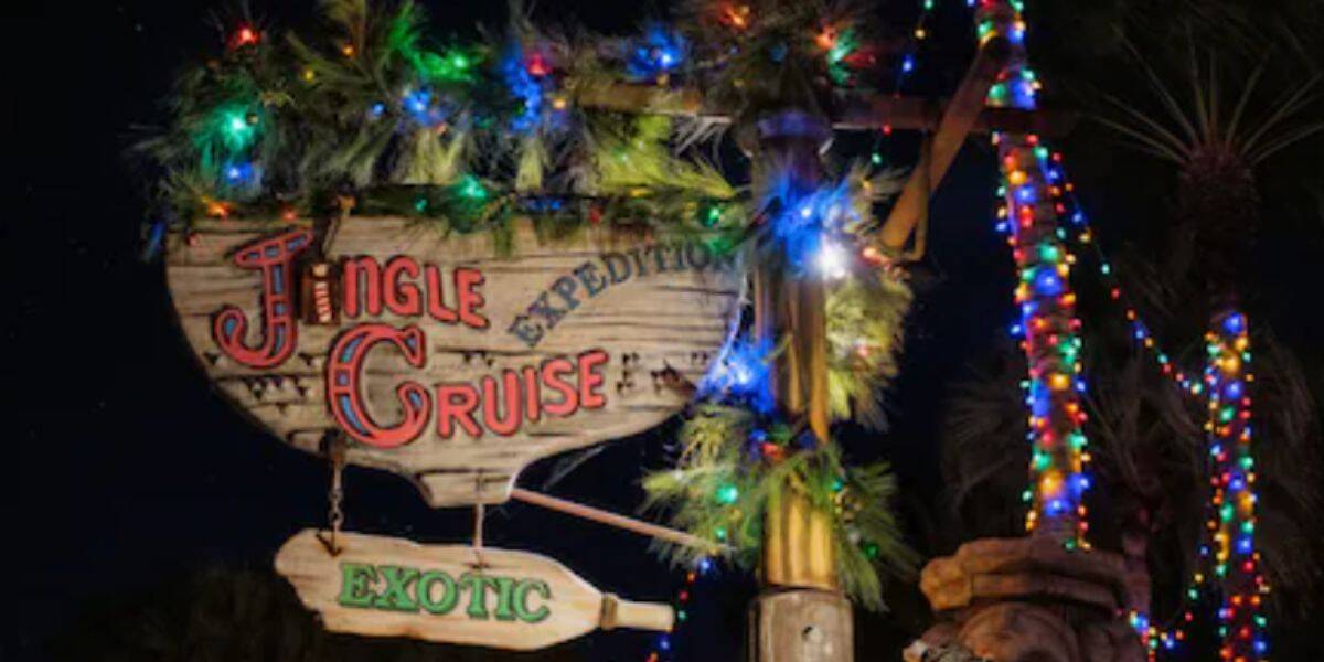 A wooden "Jingle Cruise Expedition" sign decorated with pine branches and colorful Christmas lights sparkles with Christmas cheer at night. An additional green "Exotic" sign hangs below.