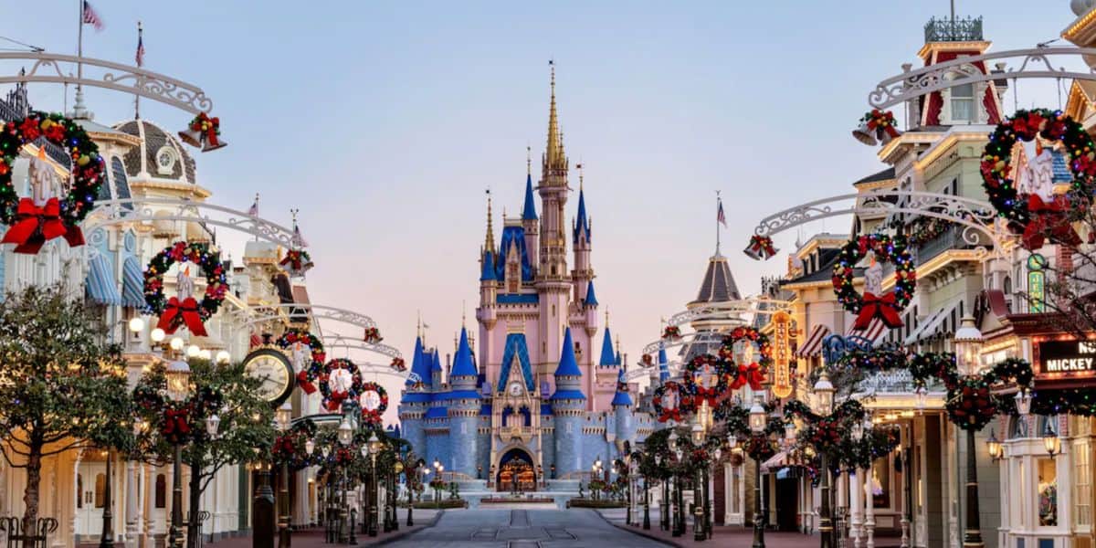 A view of Main Street at Disney World decorated with festive Christmas wreaths and garlands, leading to Cinderella Castle in the background under a clear sky.