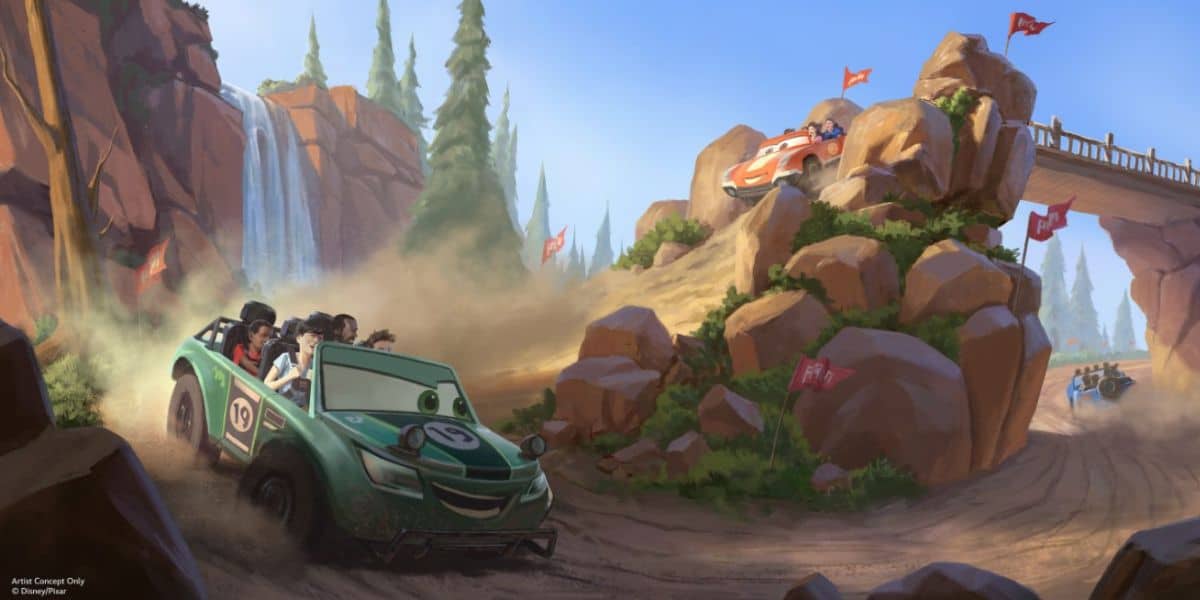 A group of people race in a green Disney car numbered 19, speeding down a dirt road by a waterfall and rocky cliffs. Other race cars zip across a bridge in the lively scene, surrounded by trees and red flags.