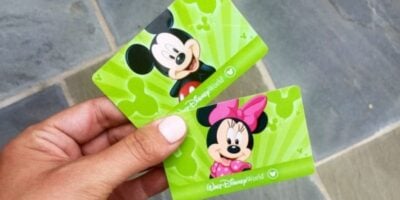 A hand holding two green Disney World tickets featuring cartoon images of Mickey Mouse and Minnie Mouse.