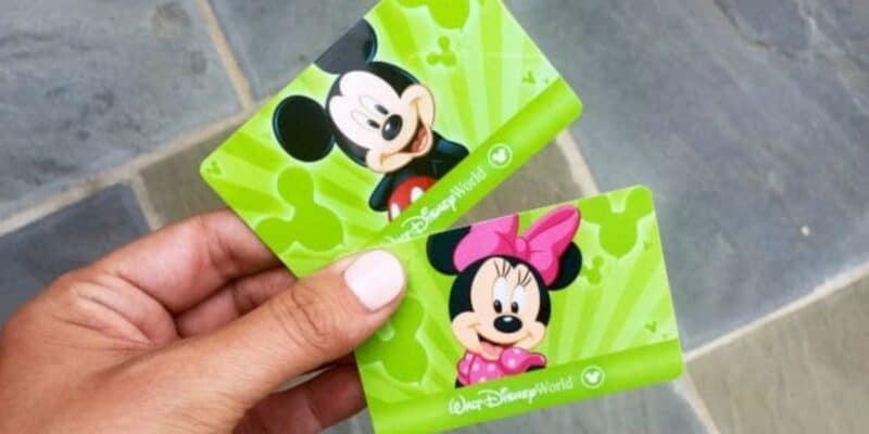 A hand holding two green Disney World tickets featuring cartoon images of Mickey Mouse and Minnie Mouse.
