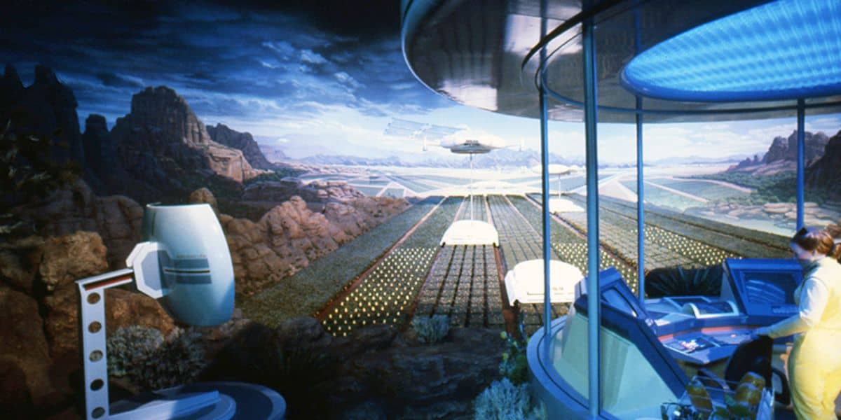 A futuristic scene shows a person in a control room overlooking vast, advanced farmland with geometric crops and hovering vehicles—reminiscent of the innovation behind the Best Disney World Ride—set against a dramatic mountainous landscape and partly cloudy sky.