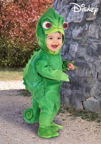 A smiling toddler wearing a bright green Pascal costume from Disney Costumes, complete with big eyes, scales, and a curled tail, stands near a stone wall outdoors. The Disney logo is in the top right corner.